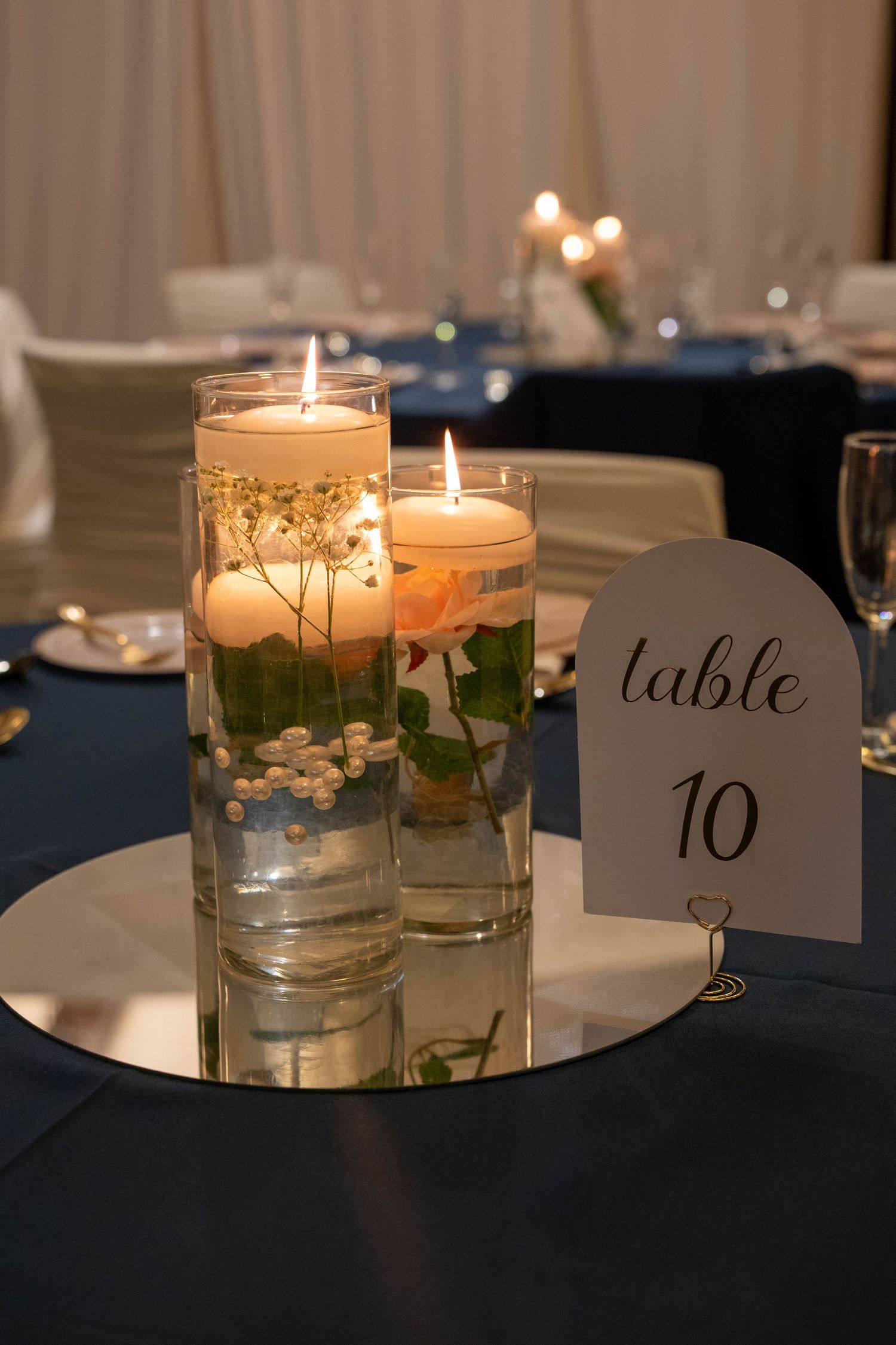Elegant wedding centerpiece with floating candles in glass cylinders beside table number 10 sign.