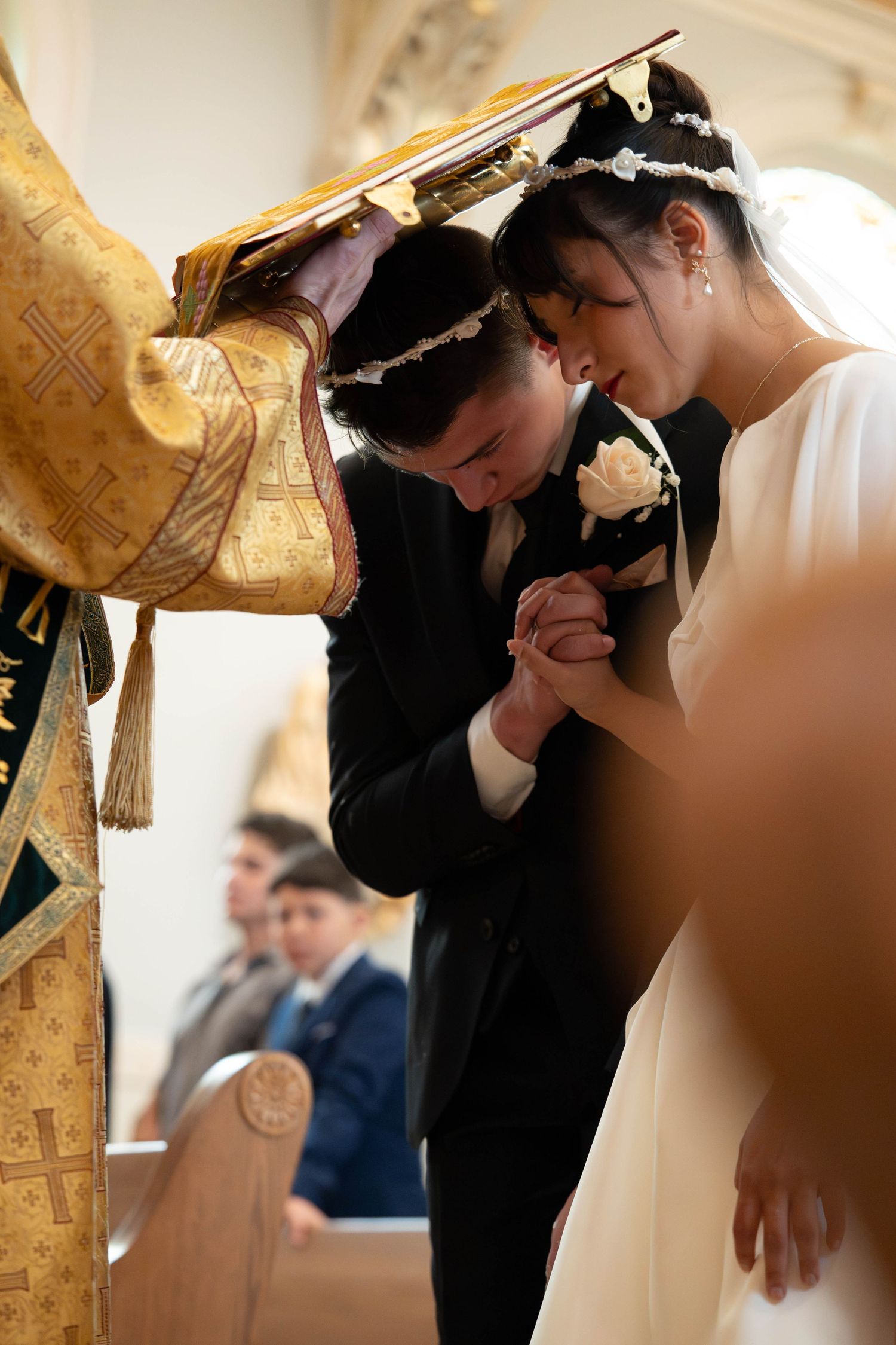Bride and groom bow their heads in prayer during an Orthodox Christian wedding ceremony.