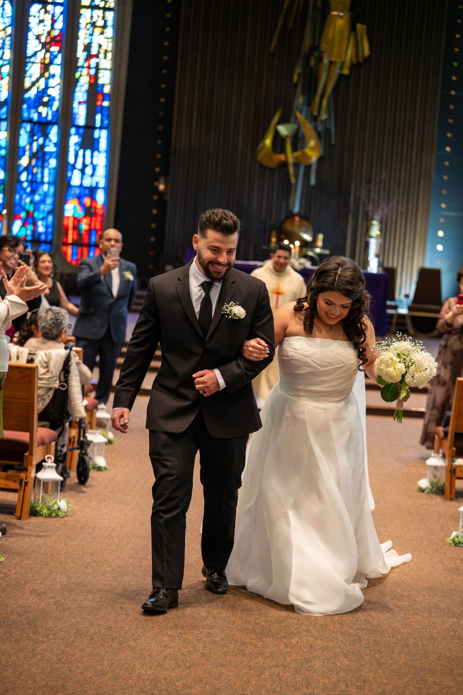 Newlywed couple joyfully walking back down church aisle after wedding ceremony as guests applaud in celebration.