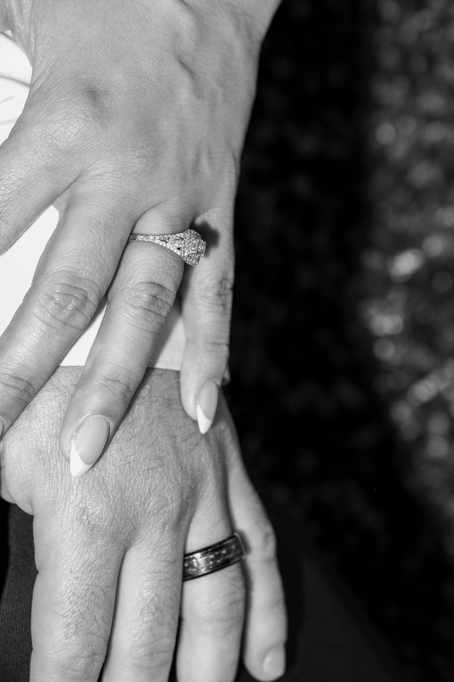 Black and white close-up of newlyweds hands showing diamond engagement ring and wedding band after ceremony.