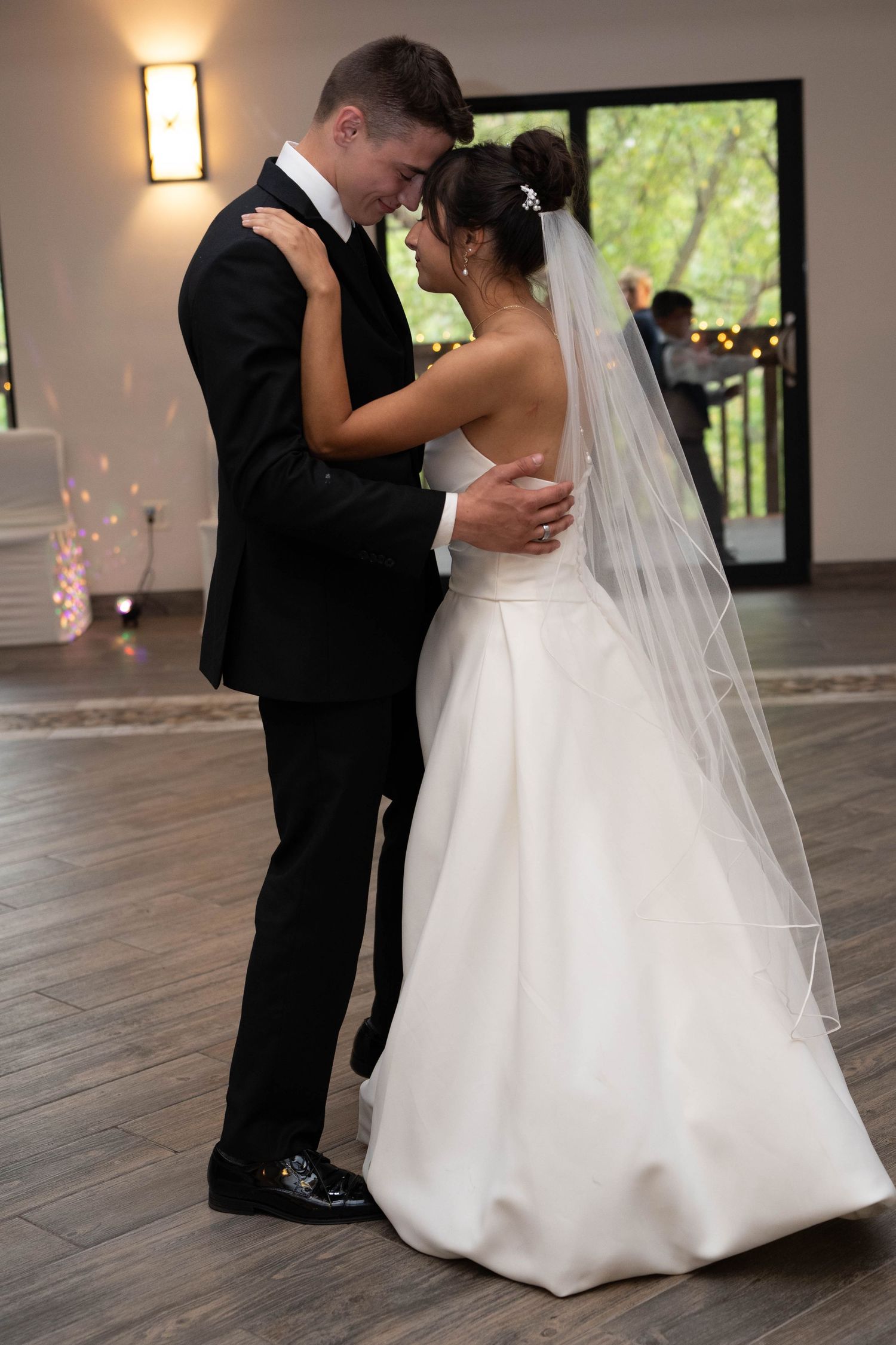 Newlyweds share romantic first dance together in elegant venue with garden views behind them.