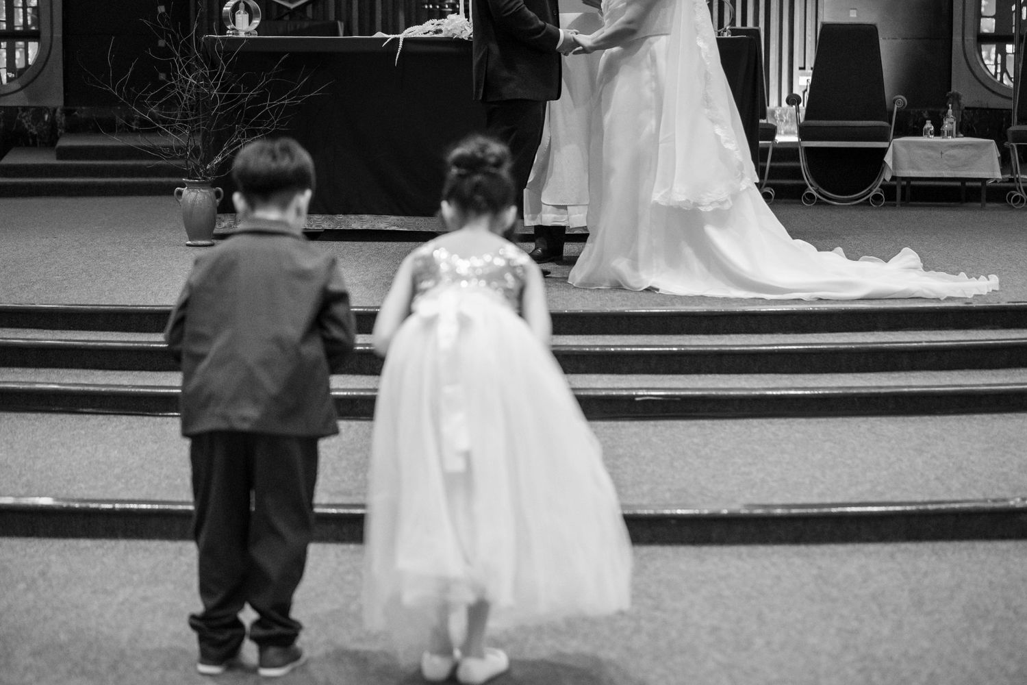 Black and white photo of flower girl and ring bearer standing at church altar during ceremony.