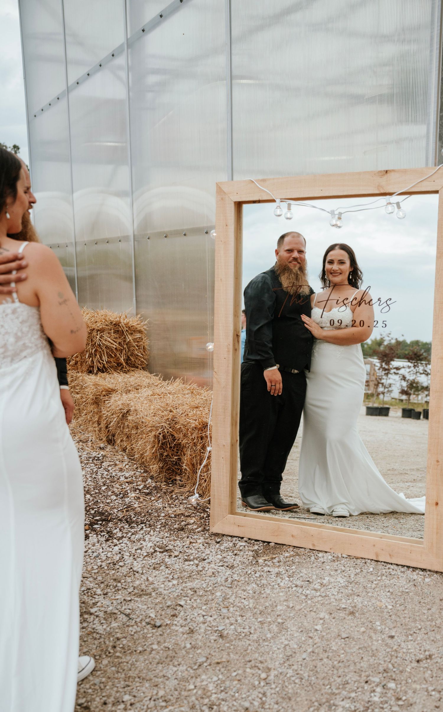 Bride and groom posing in mirror with Fischer wedding date sign near rustic hay bales.