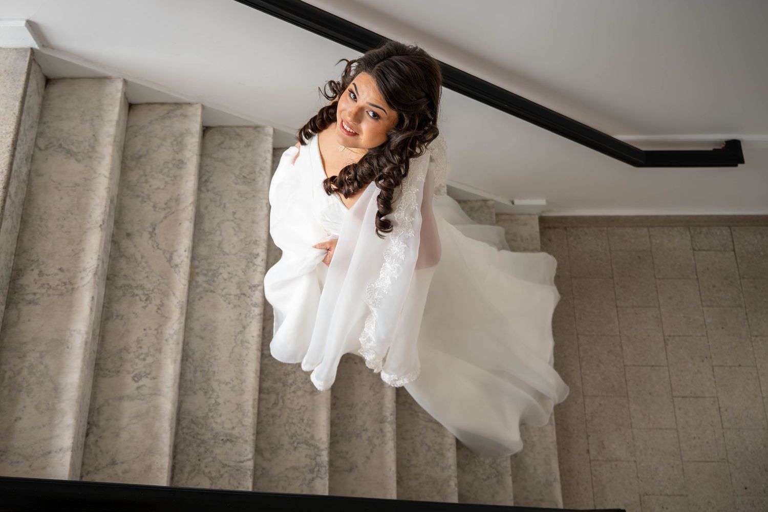 Bride twirls in white wedding gown on marble staircase, dress flowing gracefully around her.