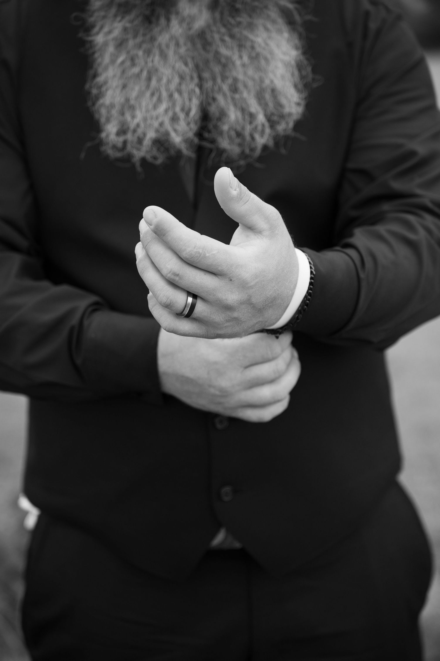 Black and white close-up of groom adjusting cufflinks with wedding ring visible.