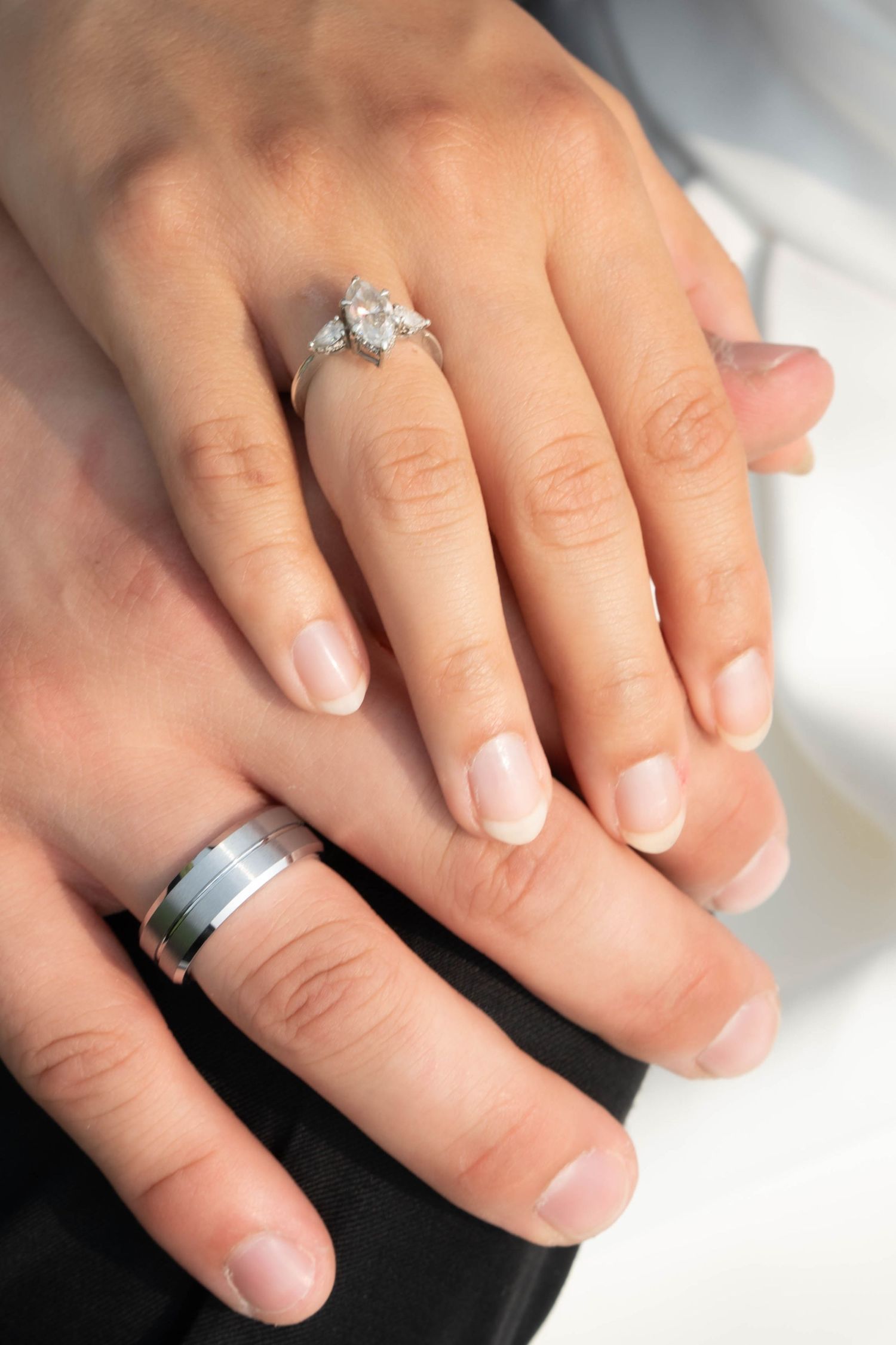 Close-up of newlyweds hands showing diamond engagement ring and silver wedding band.