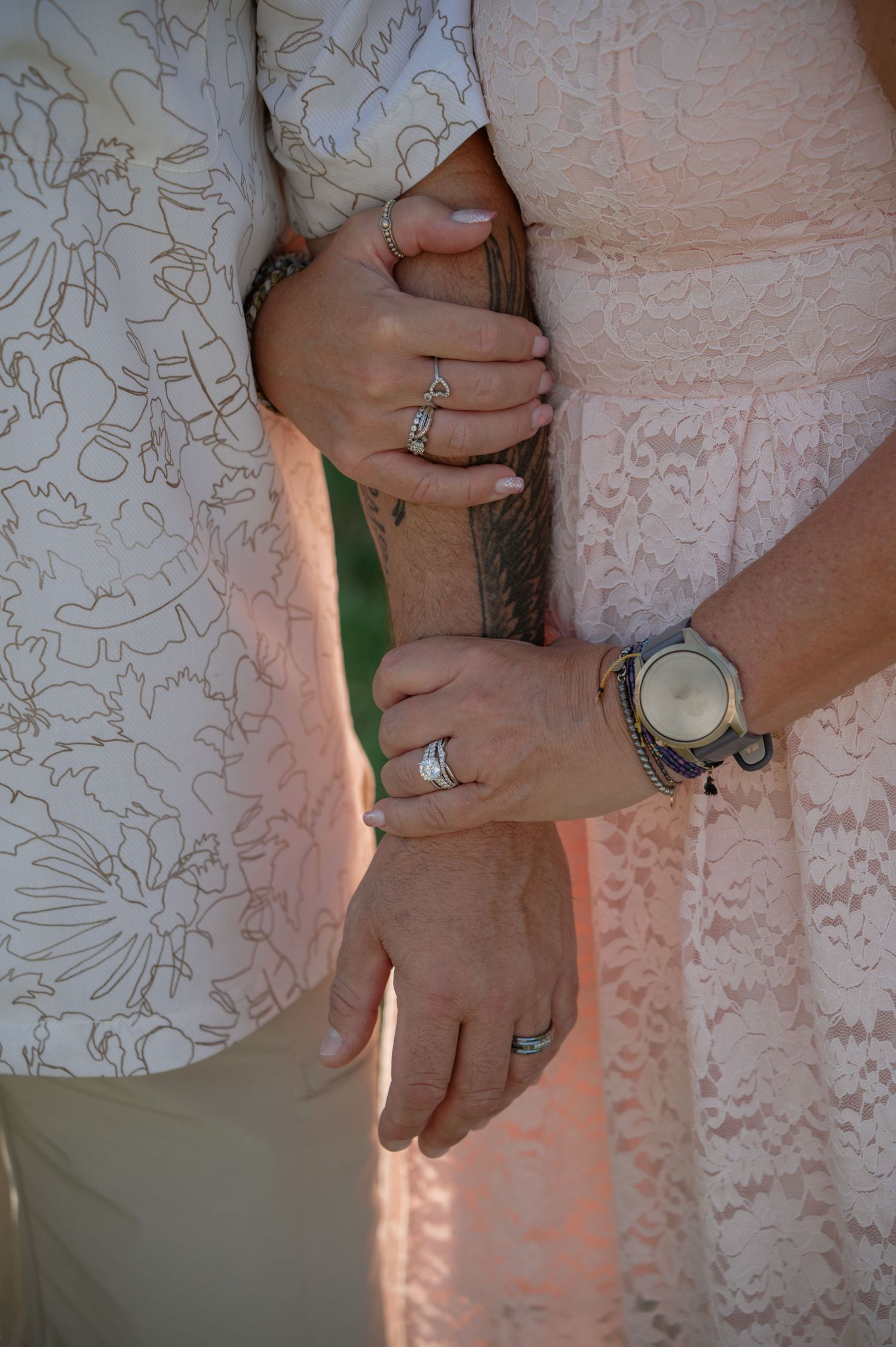 Close-up of wedding couple holding hands, showing rings, watch, and lace dress details.