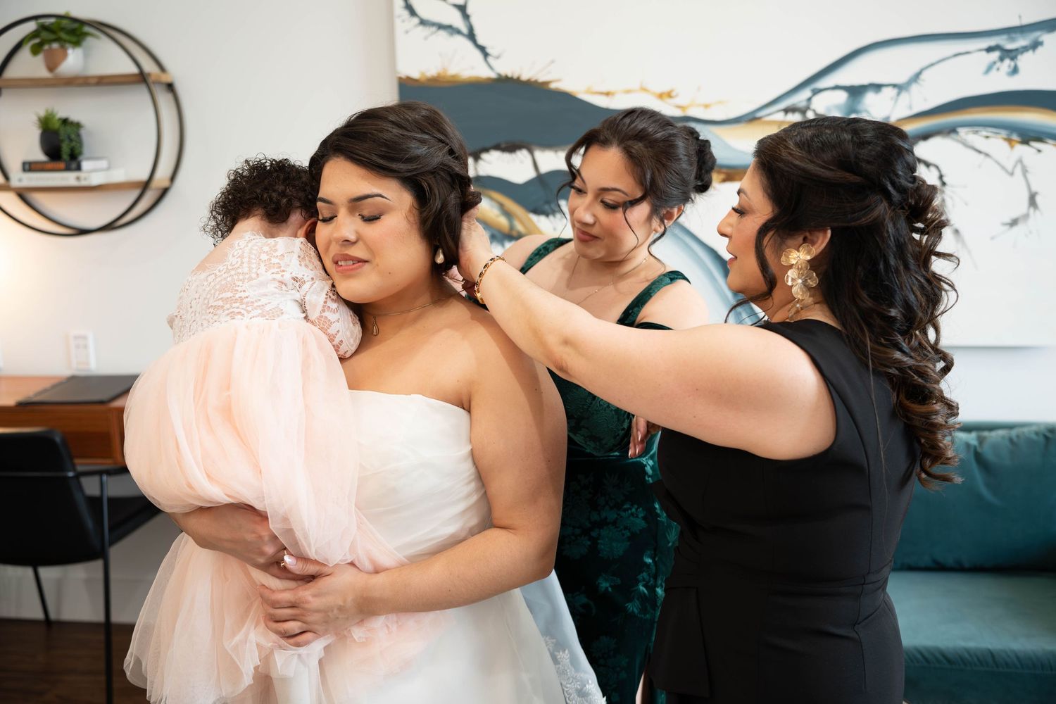 Bridesmaids and mother help bride with veil during wedding day preparations.
