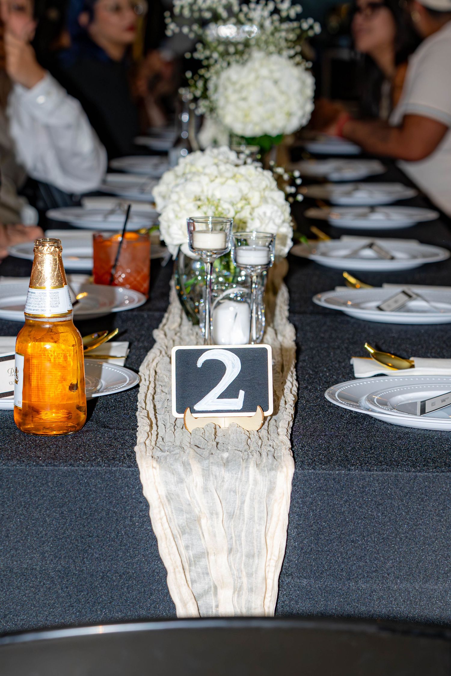 Wedding reception table number 2 with white hydrangea centerpiece on dark tablecloth with place settings.