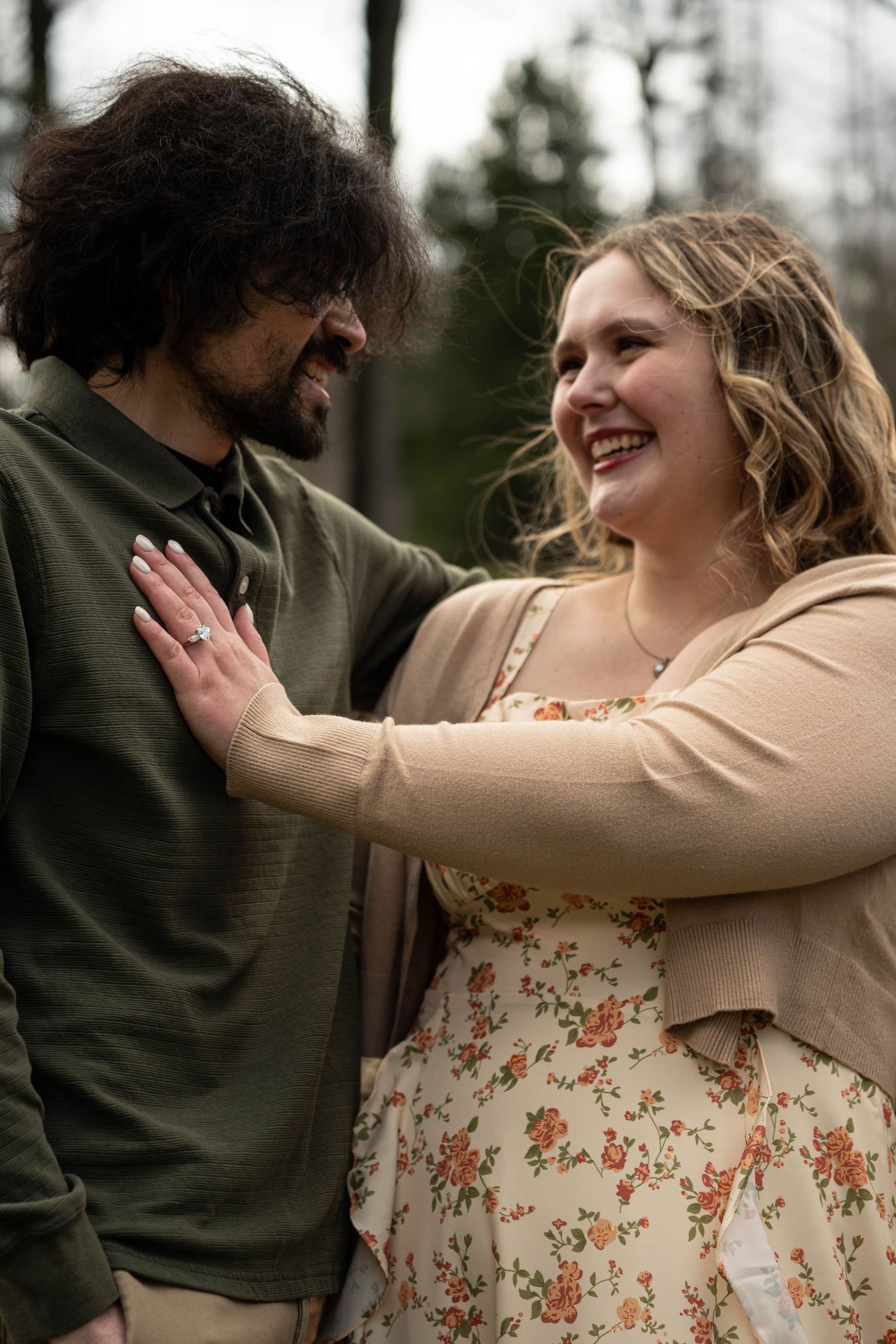 Smiling couple sharing a joyful moment outdoors, woman in floral dress placing hand on mans chest.