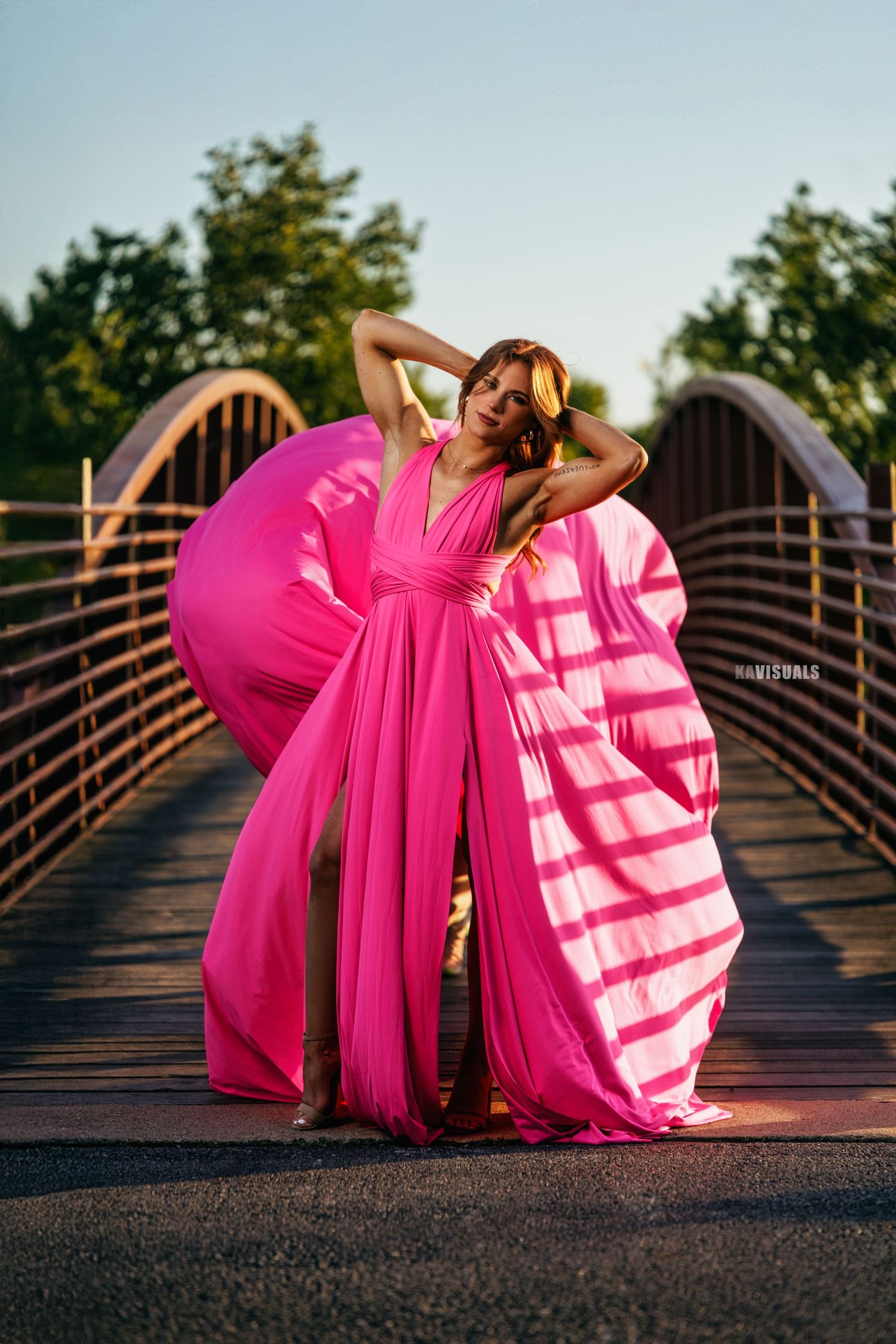 Woman in a flowing pink dress posing on a bridge with fabric dramatically billowing around her.