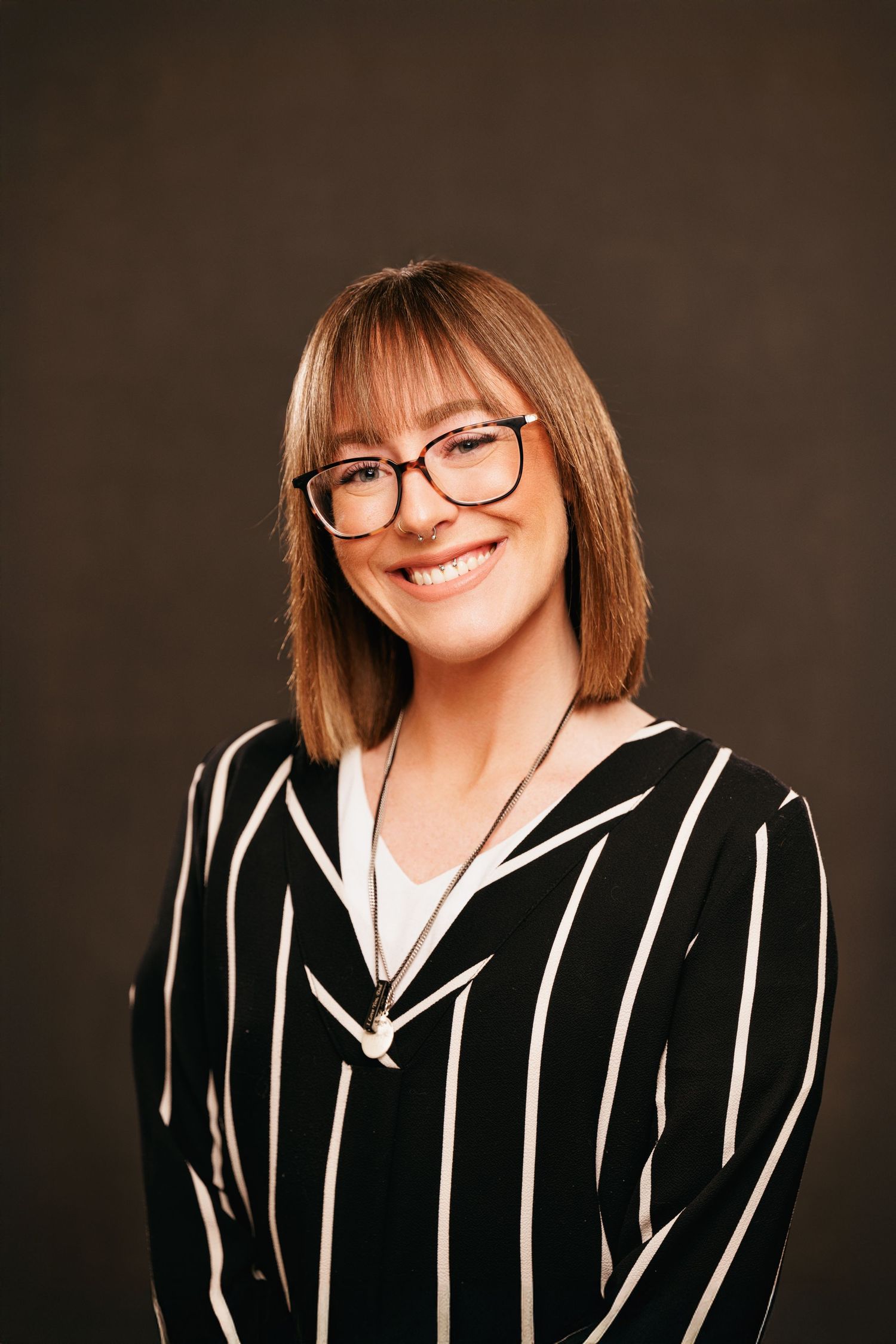 Smiling woman with glasses wearing striped blazer in professional studio portrait.
