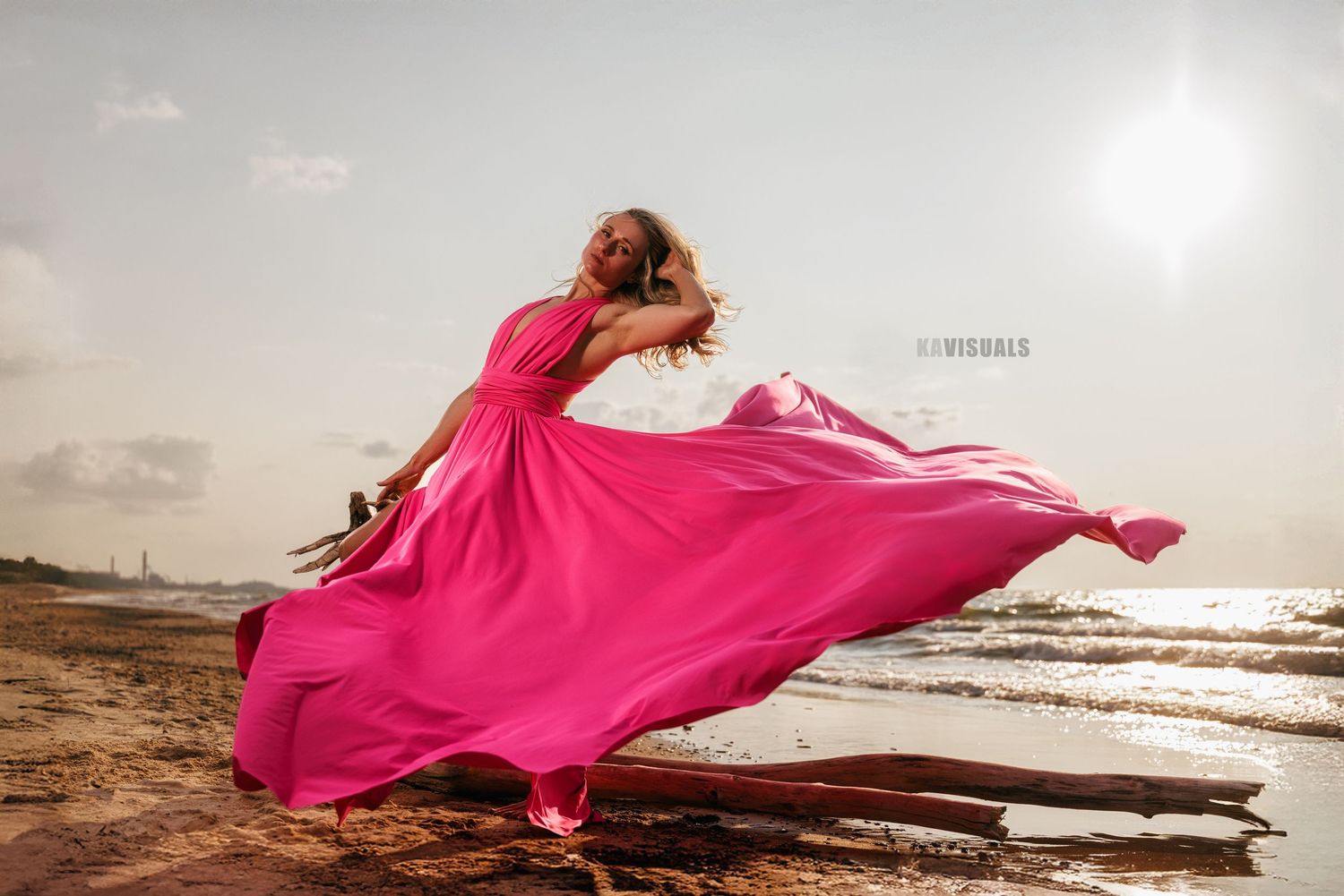 Woman in vibrant pink maxi dress spinning on a sunny beach with flowing fabric.