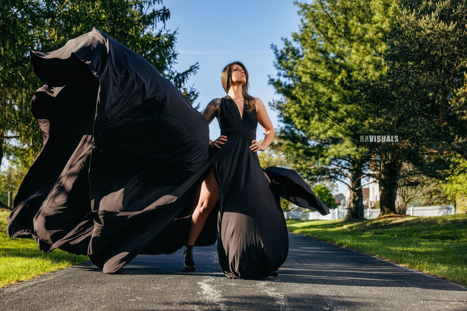 Woman in dramatic black flowing gown posing on sunlit pathway.