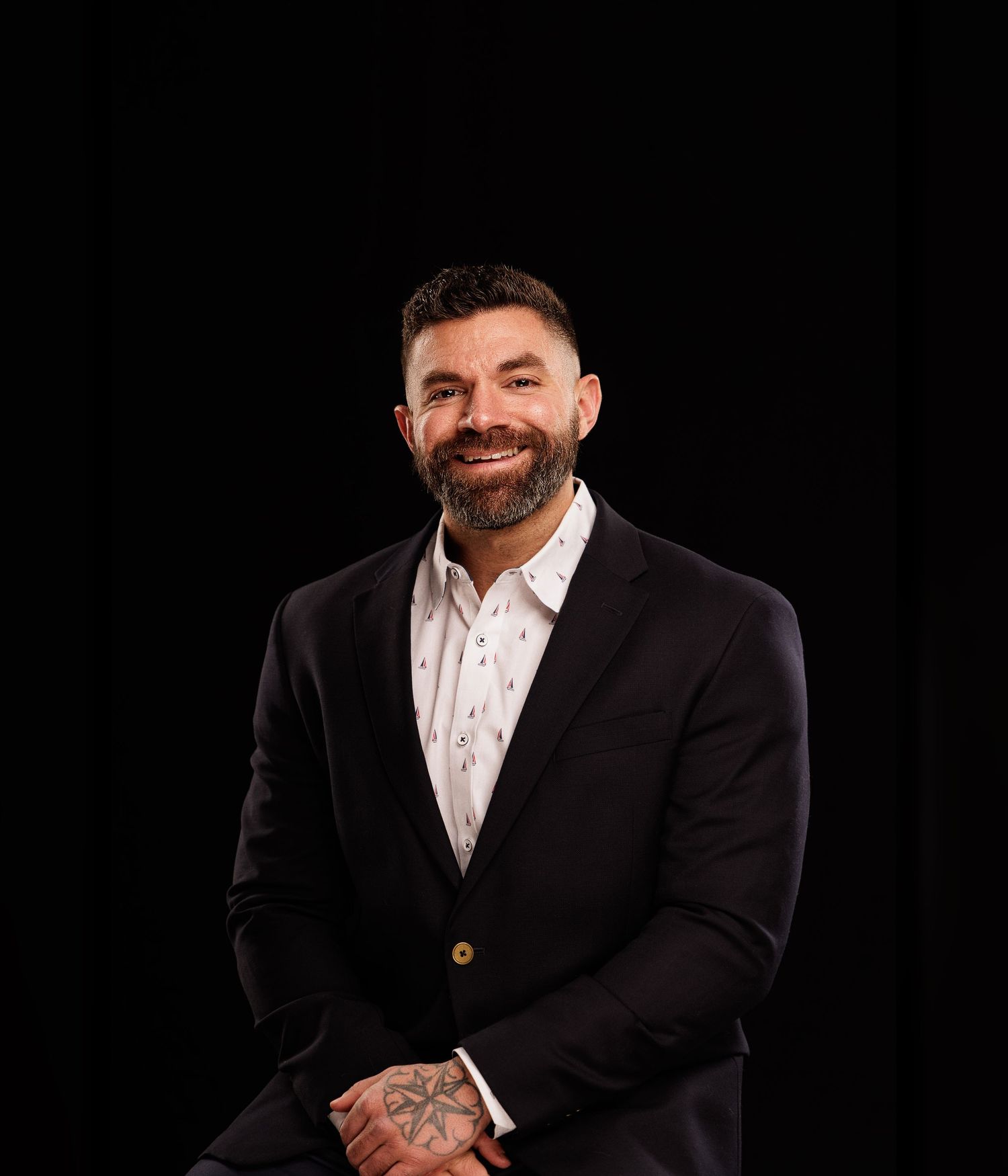 Professional portrait of a smiling man in a dark blazer and white shirt against a black background.