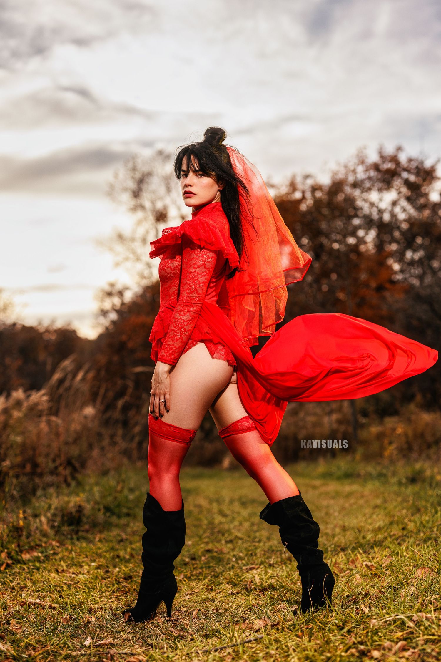Woman in flowing red lace dress with veil and thigh-highs posing outdoors in autumn.