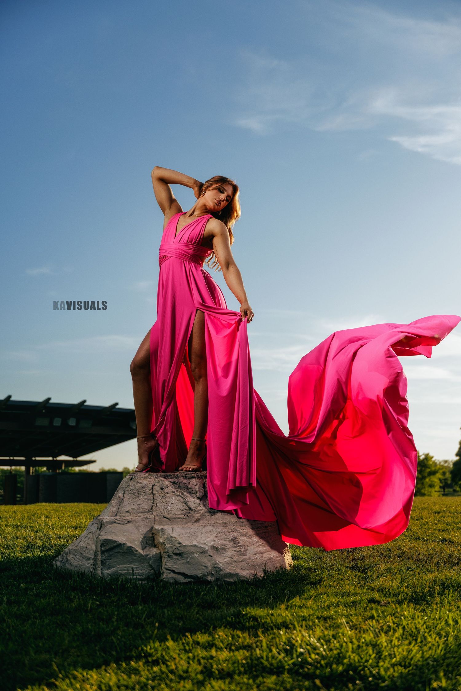 Woman in a flowing hot pink gown standing on a rock with fabric billowing in the wind.
