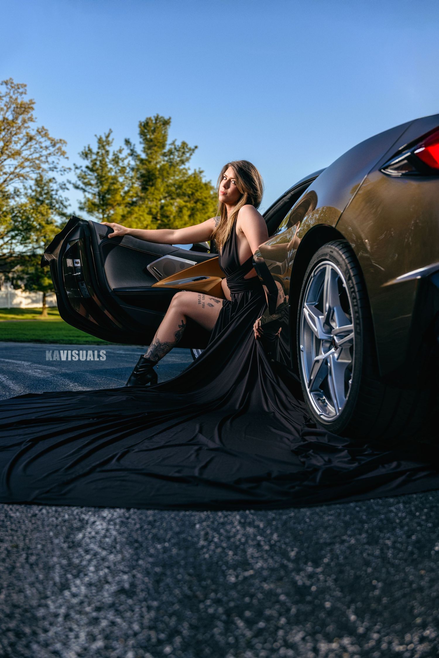 Woman in black gown exiting luxury sports car on open road.