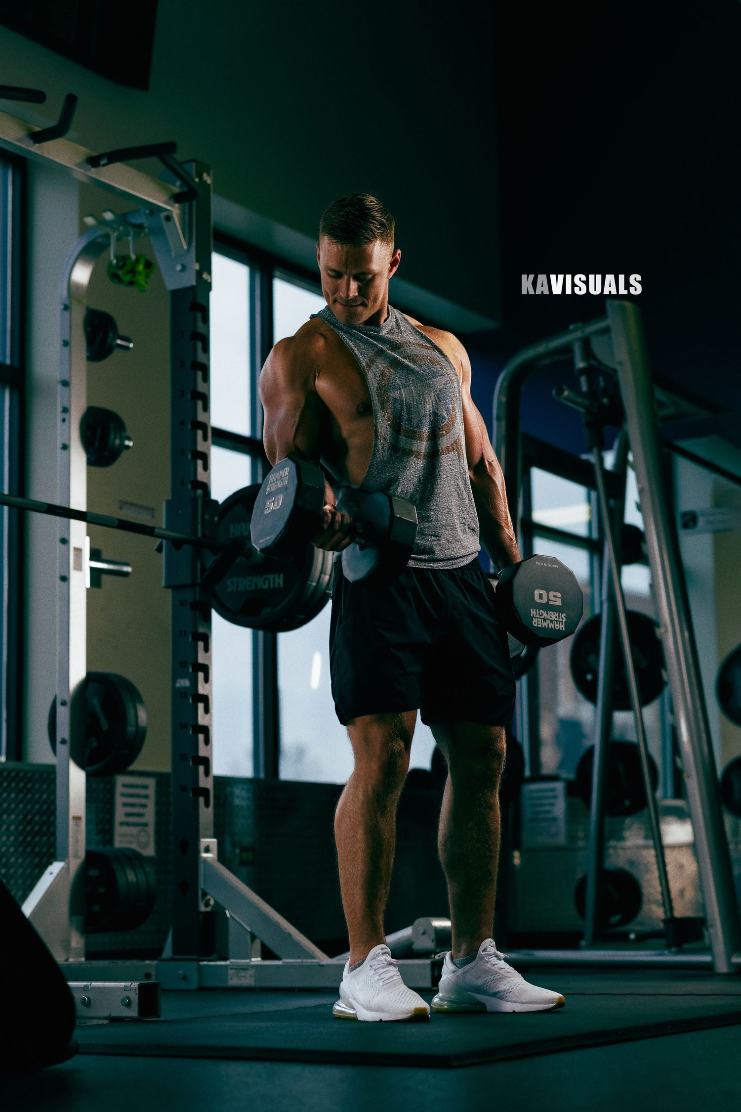 Muscular man lifting heavy dumbbells during an intense workout session in a dark gym.