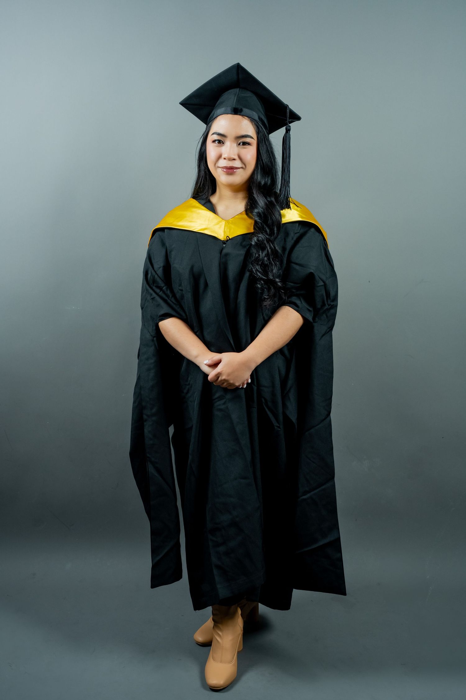 Graduation photos of someone wearing a black academic gown and cap posing against a grey studio backdrop.
