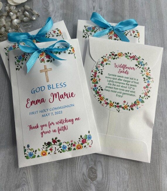 White First Holy Communion favor tags with blue ribbons and floral designs arranged in a row on gray background.