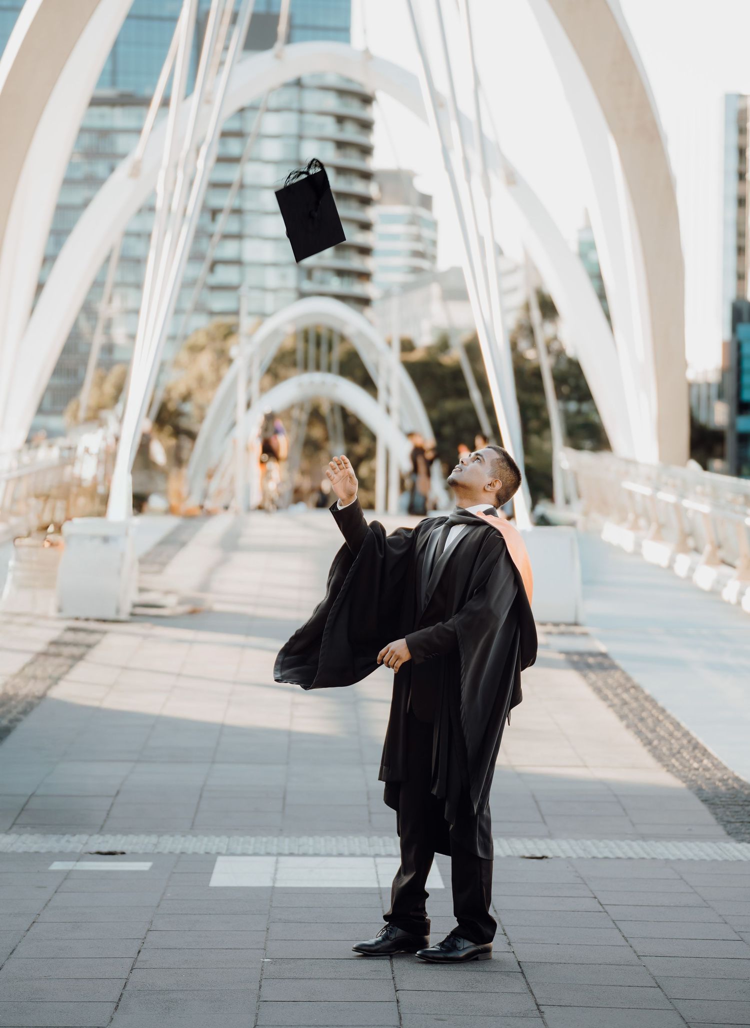 A series of five photos showing graduates in black caps and gowns celebrating on a modern bridge walkway.