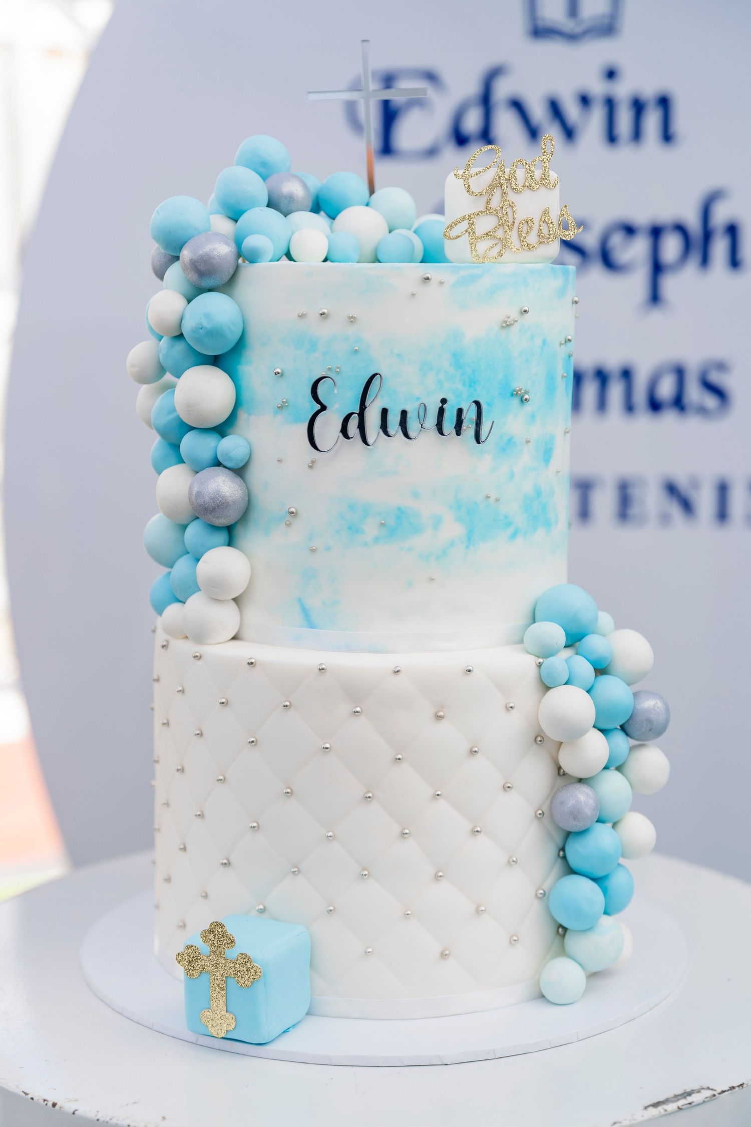 White and blue christening cake decorated with bubble-like fondant balls and delicate gold accents for a baptism celebration.