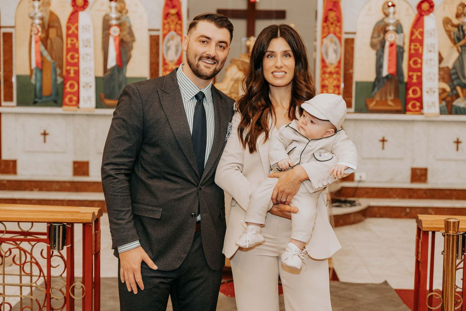 A couple stands together in a church with red and white decor visible in the background.