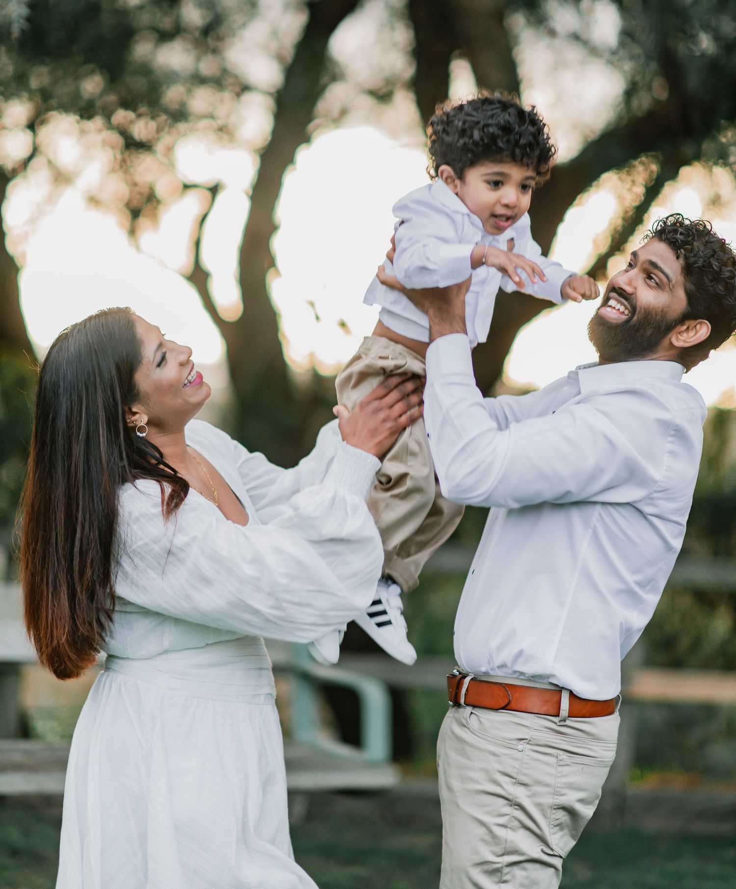 A family in white outfits dances and plays together in a sunlit outdoor setting.