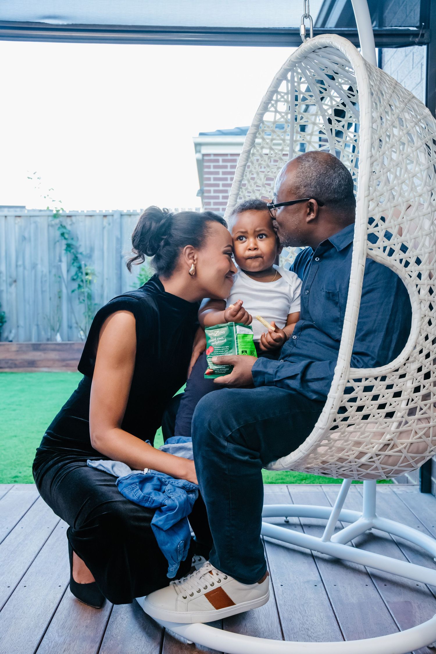 Family sharing tender moments together on a wooden deck with hanging wicker chairs in the background.