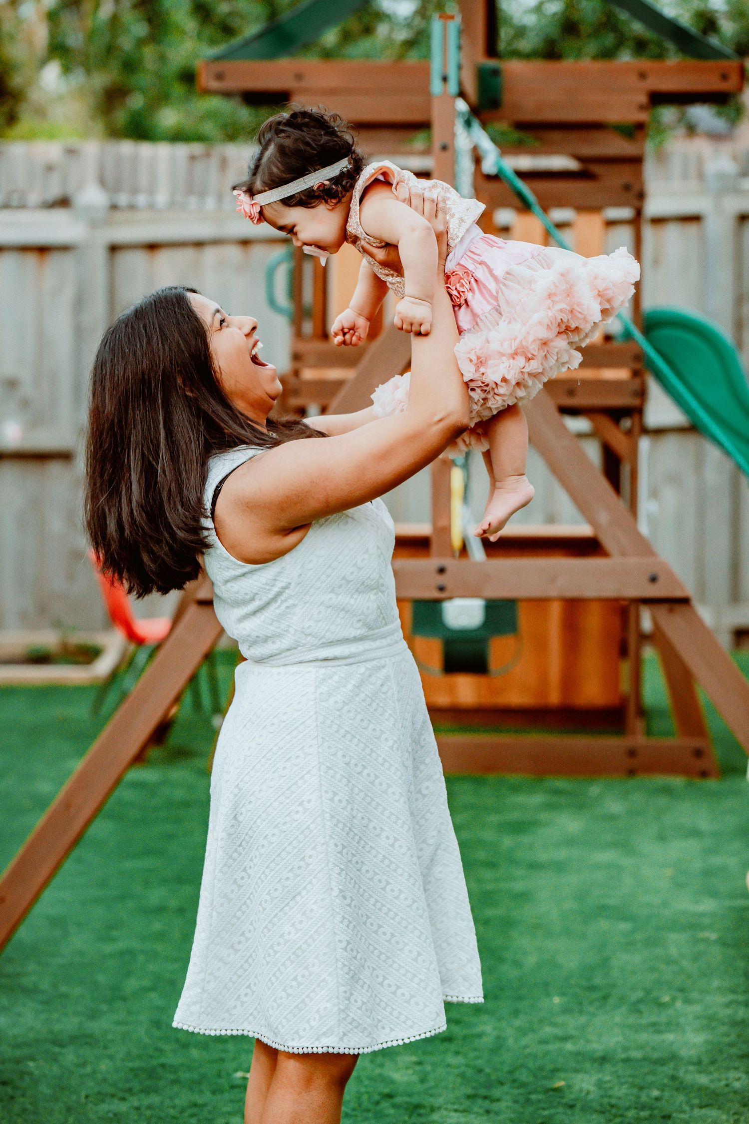A sequence of four photos showing joyful moments between parent and child playing in a backyard with playground equipment.