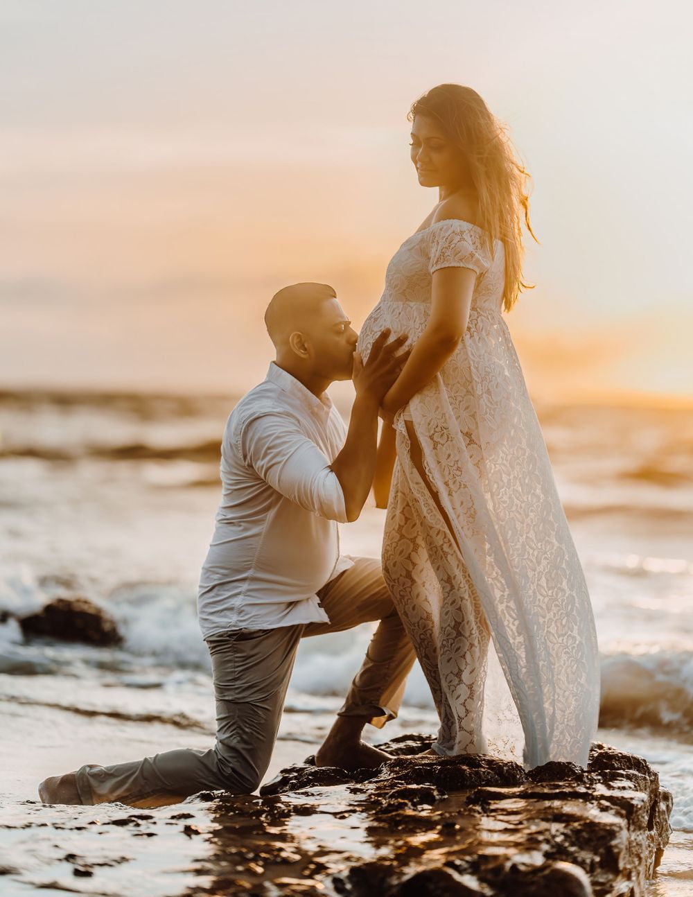 A romantic beach proposal scene at sunset with waves crashing on rocky shore.