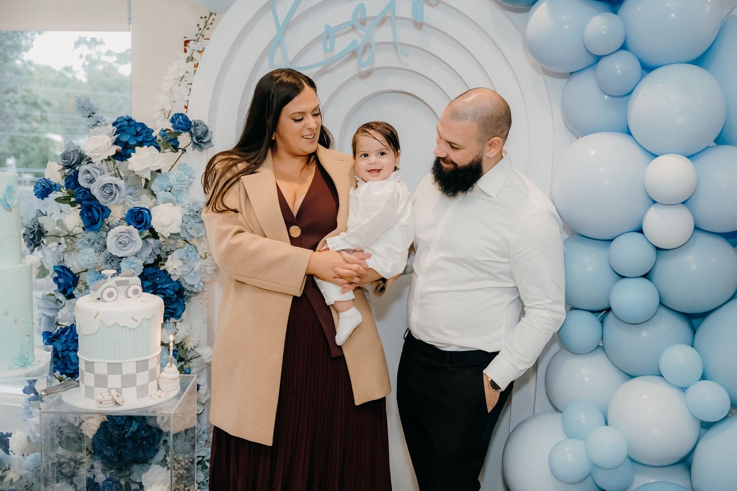A blue and white balloon arch decorates an elegant party setting with people gathered to celebrate.