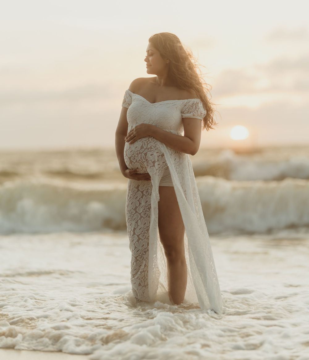A romantic beach wedding photo showing a flowing white dress against ocean waves at sunset.