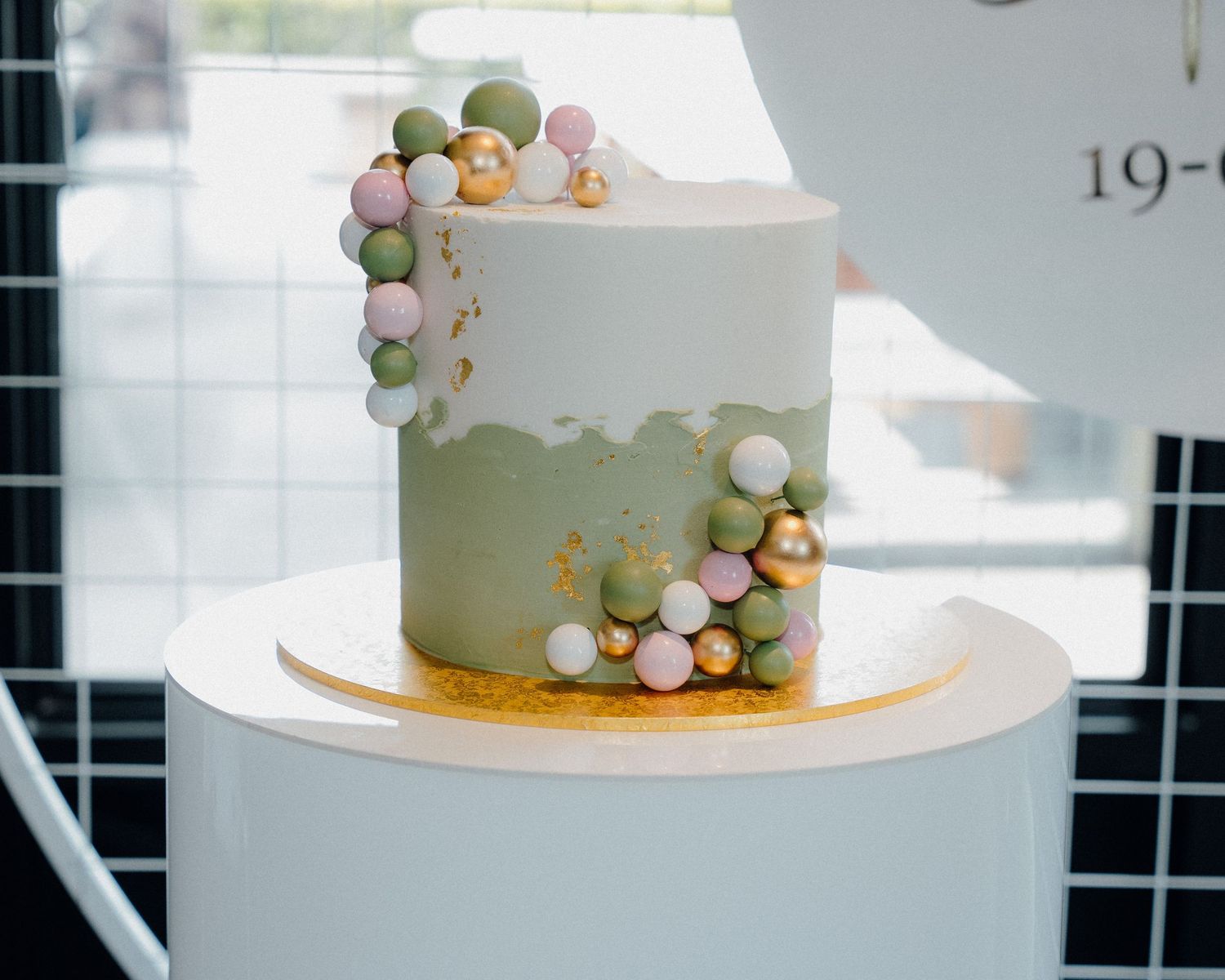 A modern white wedding cake decorated with pastel green, pink and gold bubble-like ornaments arranged in clusters.