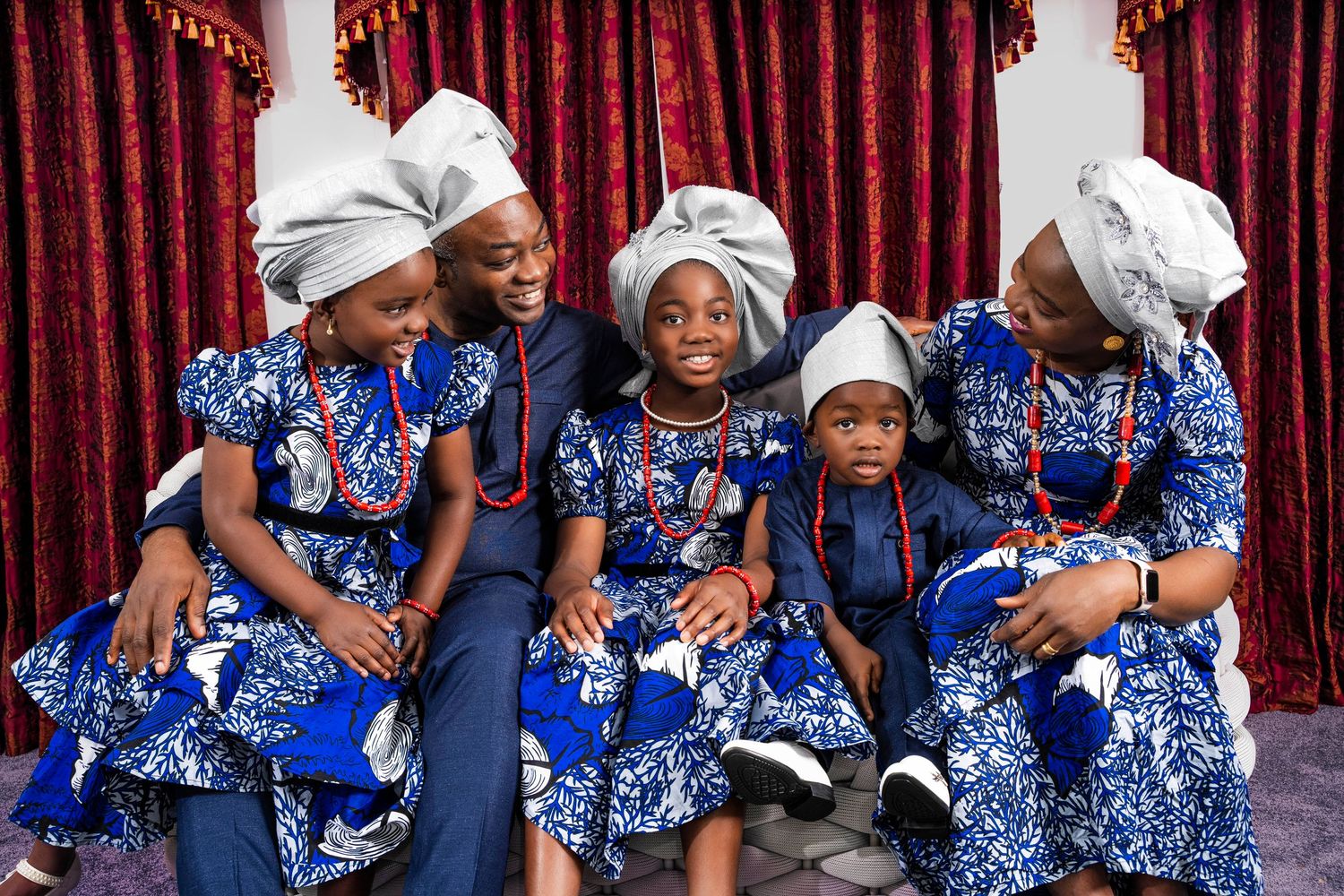 Group of people wearing matching blue and white floral outfits pose together in front of red curtain.