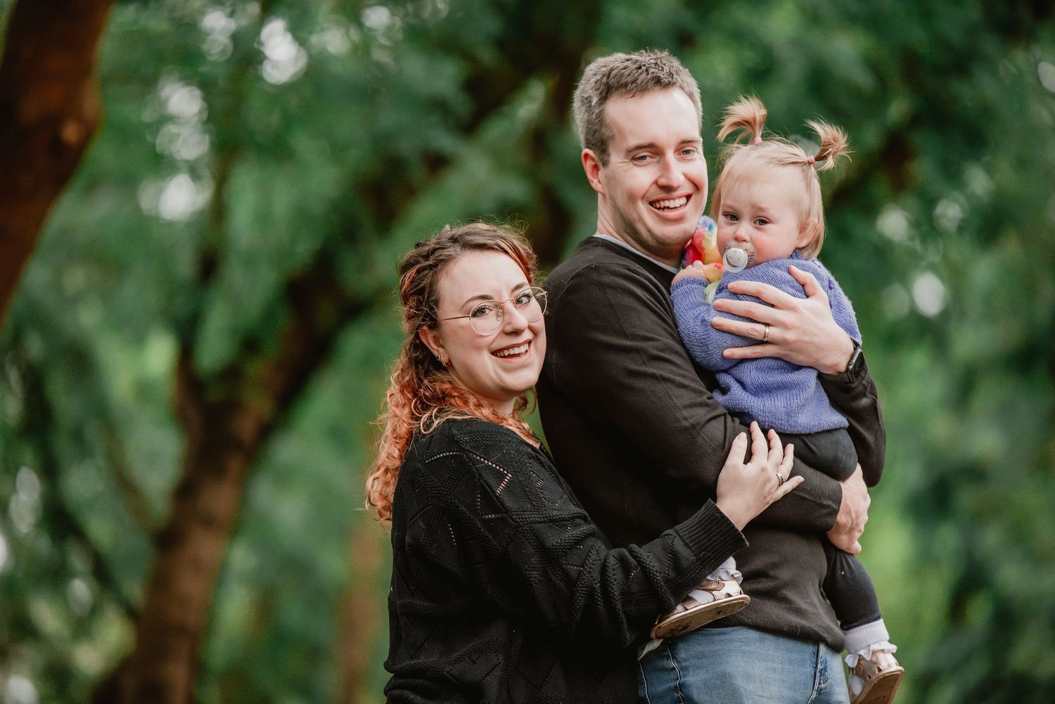 A couple and their baby share joyful moments in a lush outdoor setting during a family photo session.
