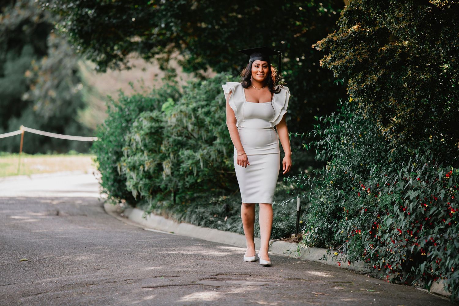 A bride in a white dress walks down a garden path with lush greenery on both sides.