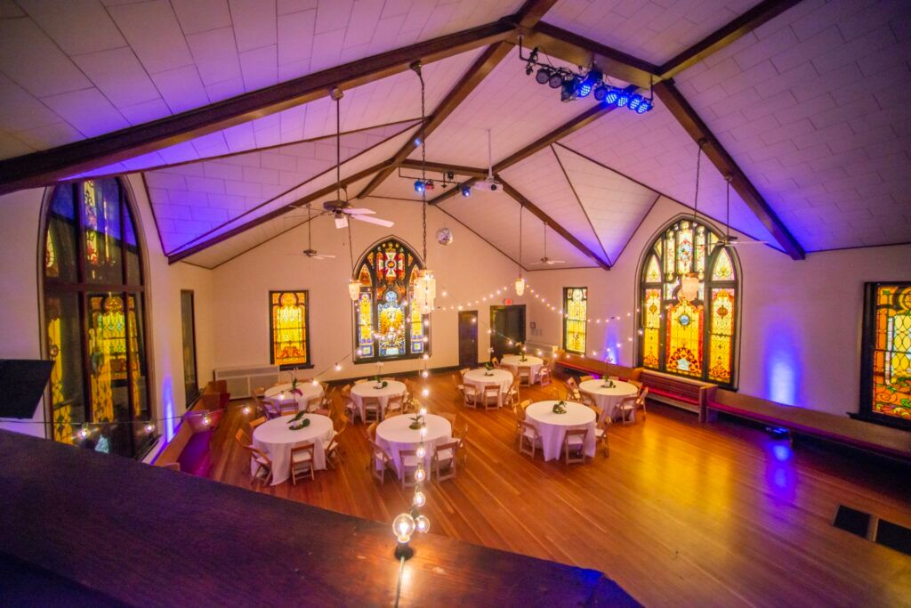 A wedding reception venue with purple uplighting, stained glass windows, and elegant table settings.
