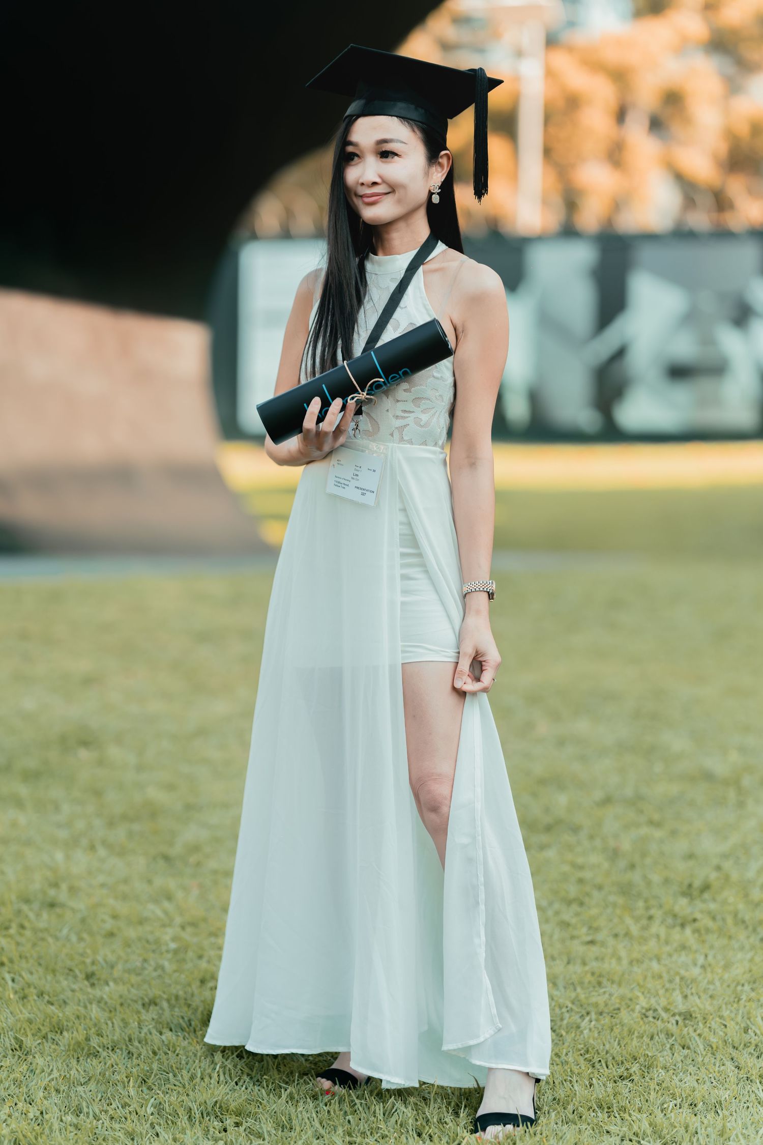 Graduate in white dress poses in grassy field during sunset photoshoot.