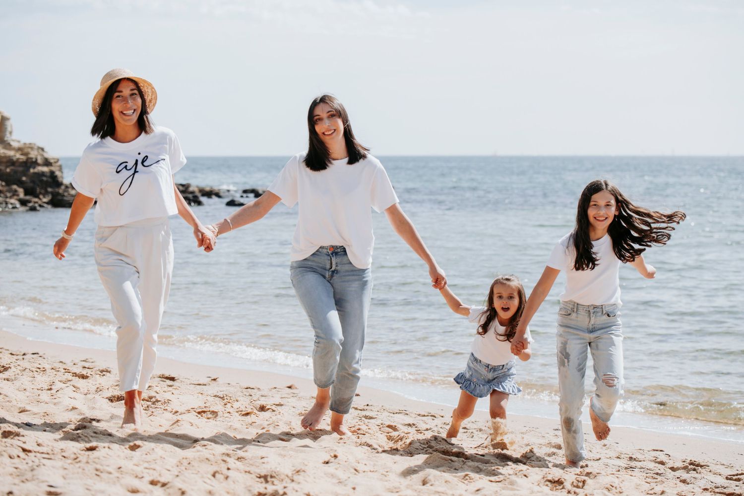 A family holding hands and walking together along a sunny beach shoreline with waves in the background.