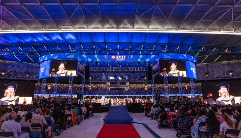 Wide panoramic view of a large indoor arena with blue lighting and stadium seating during an event.