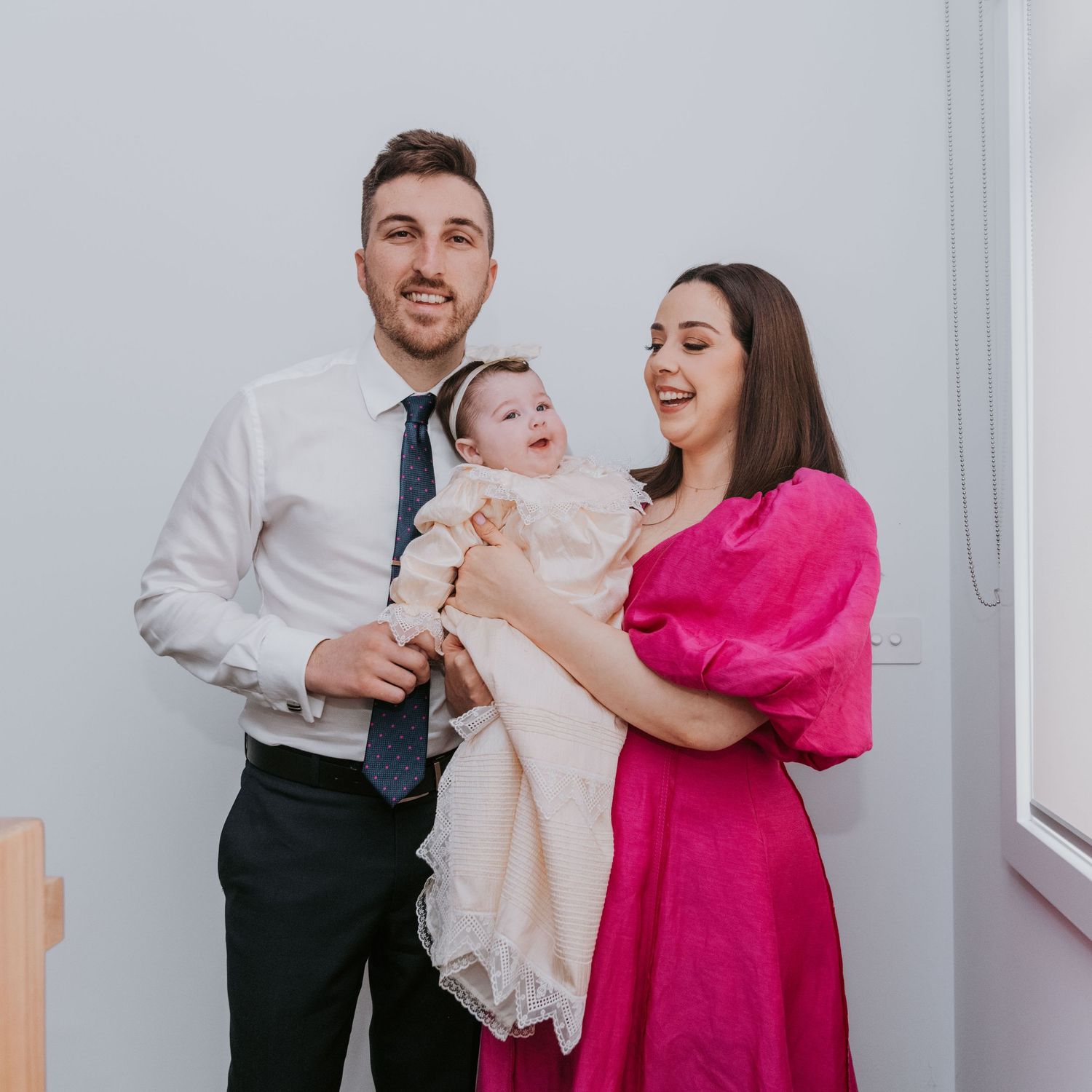 A couple in formal attire sharing tender moments with their baby in a bright white room.