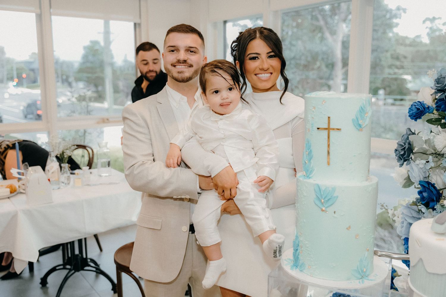Family celebrates special occasion with elegant blue and white baptism cake at reception venue.