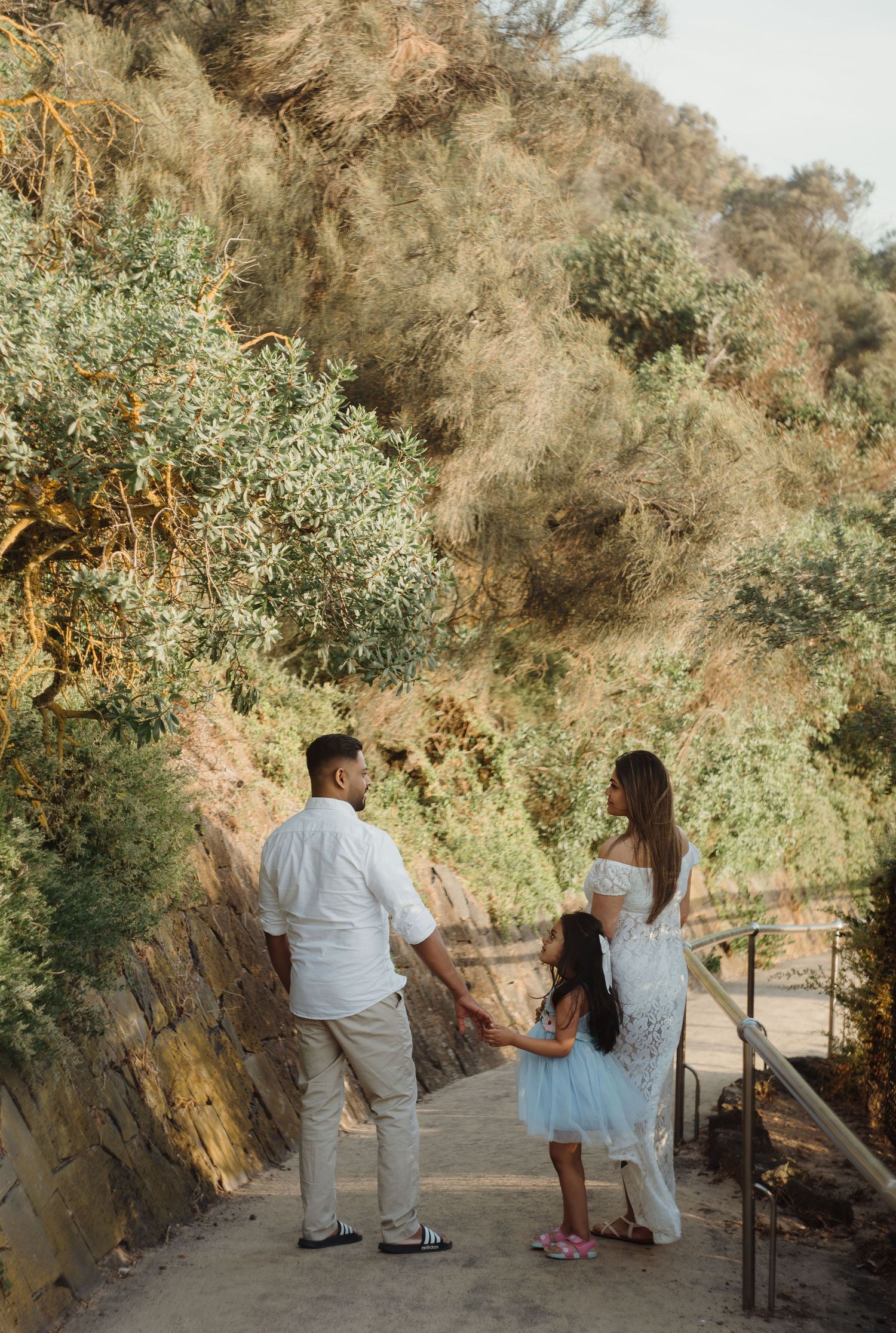 A couple walks together on a scenic hiking trail surrounded by lush greenery and rocky cliffs.