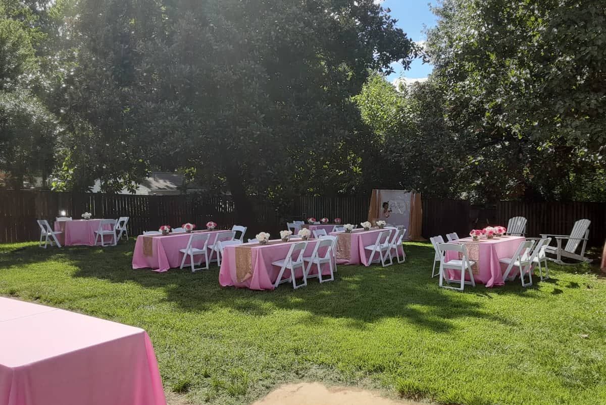 Outdoor garden wedding setup with white folding chairs and pink decorations arranged on a grassy lawn in summer.