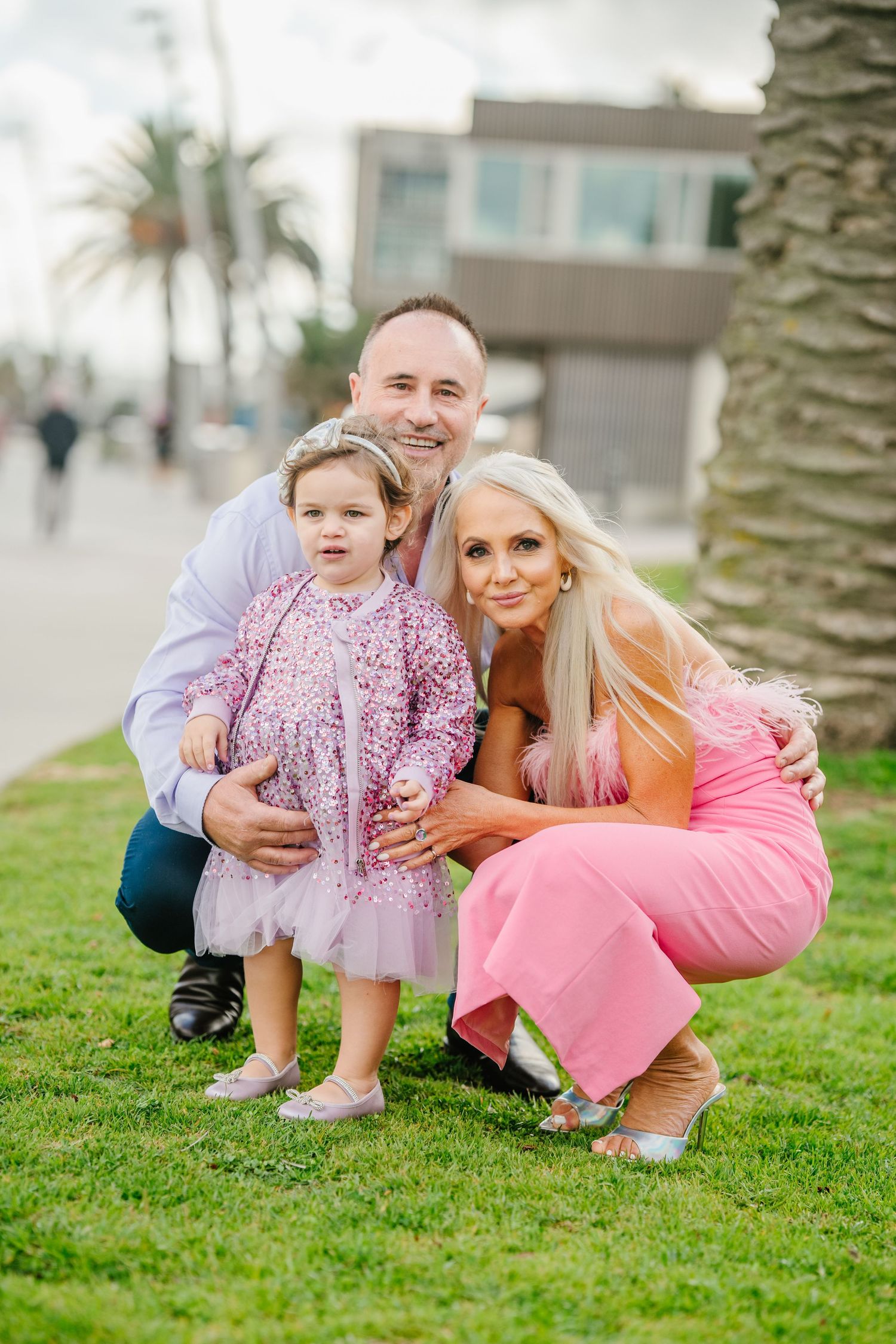 Three candid outdoor photos of a family posing together on green grass with palm trees in the background.