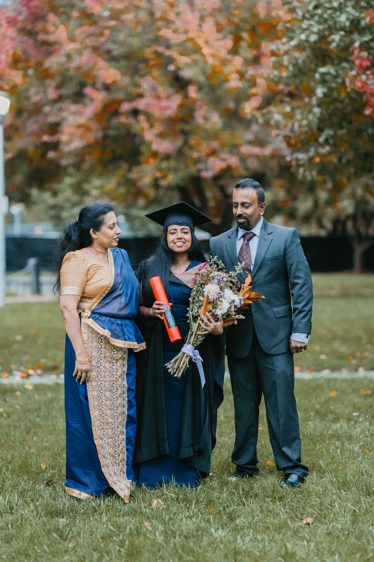 A group of people in formal attire share a joyful moment on a grassy lawn with autumn foliage in the background.