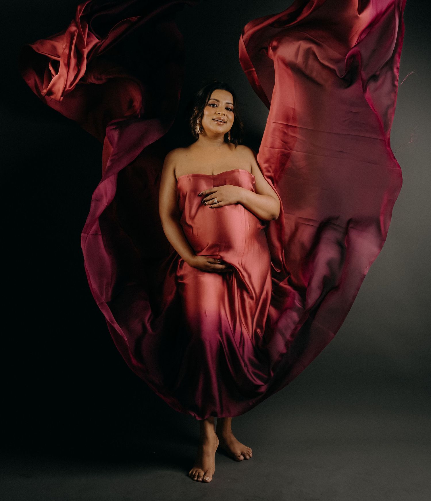 A flowing burgundy dress billows dramatically against a dark background in an artistic fashion photograph.