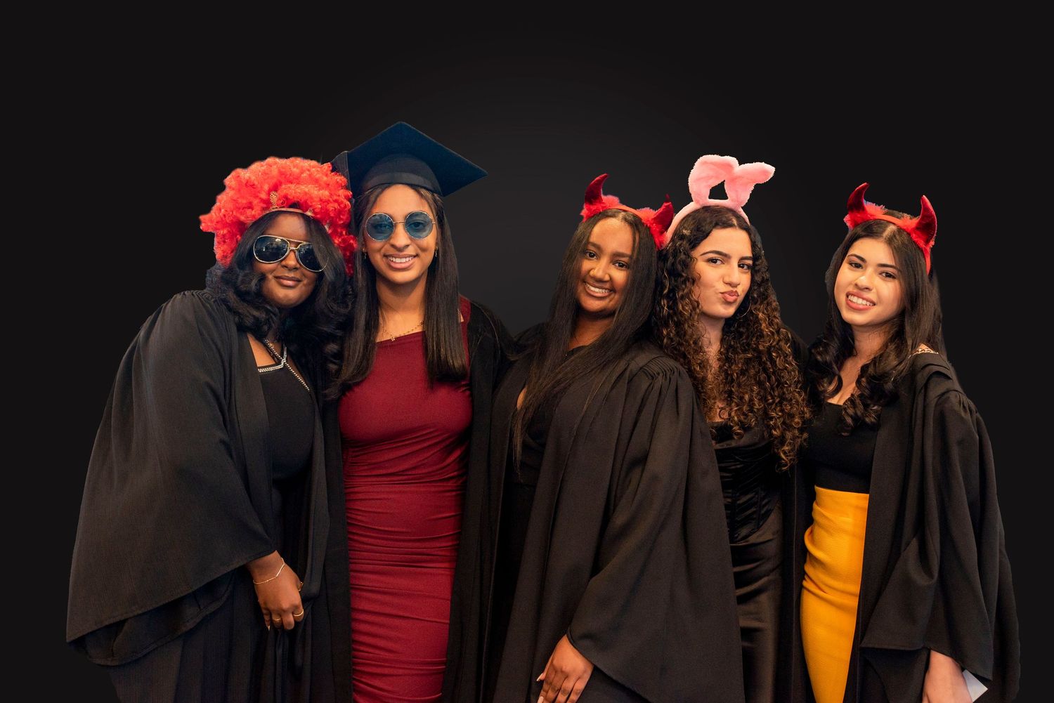 A group of graduates in black caps and gowns pose together with smiles during a graduation ceremony celebration.